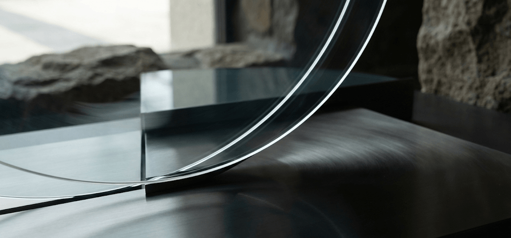 Modern glass sculpture with curved lines on a textured stone background, showcasing contemporary art design.