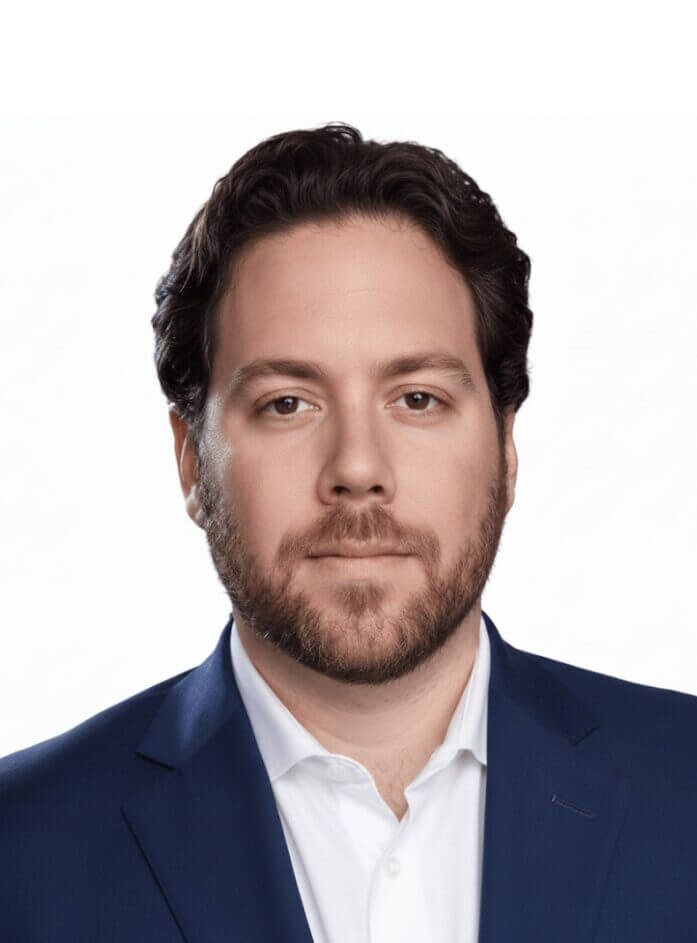 Portrait of a man in a blue suit and white shirt against a plain background, professional headshot.